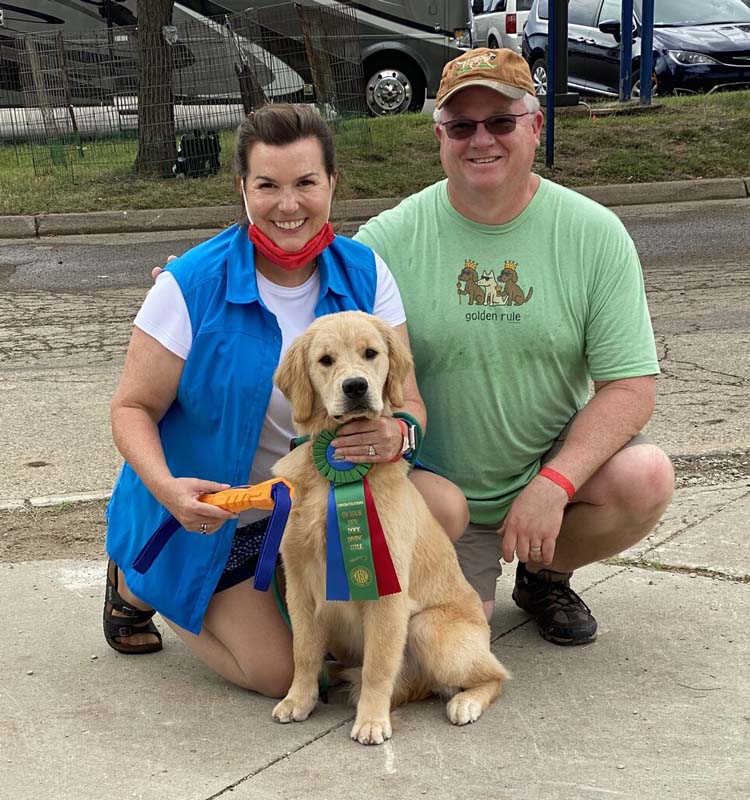 Man and woman with young golden retriever and green, blue and red ribbon
