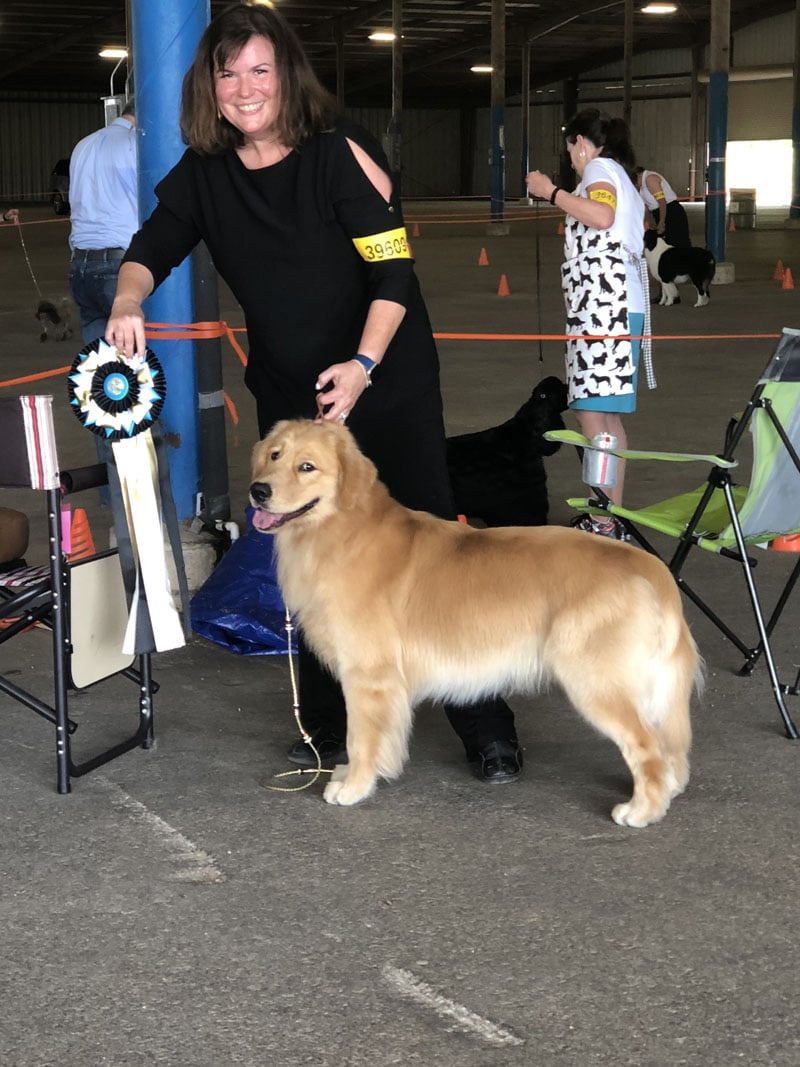 Woman in black pant suit with golden retriever showing off ribbon award