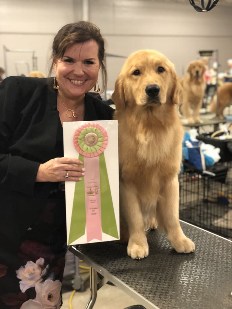 Woman holding an award ribbon next to a young golden retriever