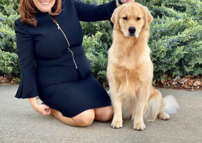 Woman in black suit with a beautiful golden retriever sitting behind multi-colored ribbons