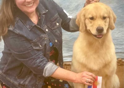 Beautiful golden retriver sitting with a smiling woman holding 2 ribbons
