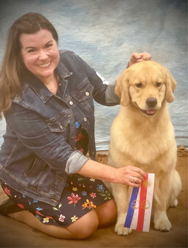 Beautiful golden retriver sitting with a smiling woman holding 2 ribbons