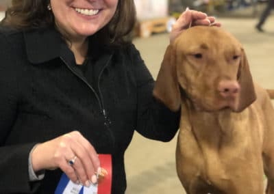Woman smiling holding ribbons next to a beautiful Vizsla