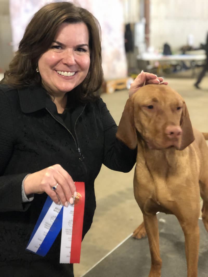 Woman smiling holding ribbons next to a beautiful Vizsla