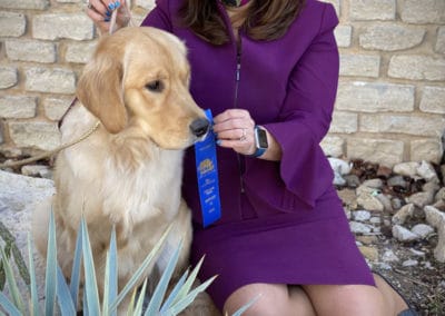 Woman in purple suit holding blue ribbon next to a golden retriever